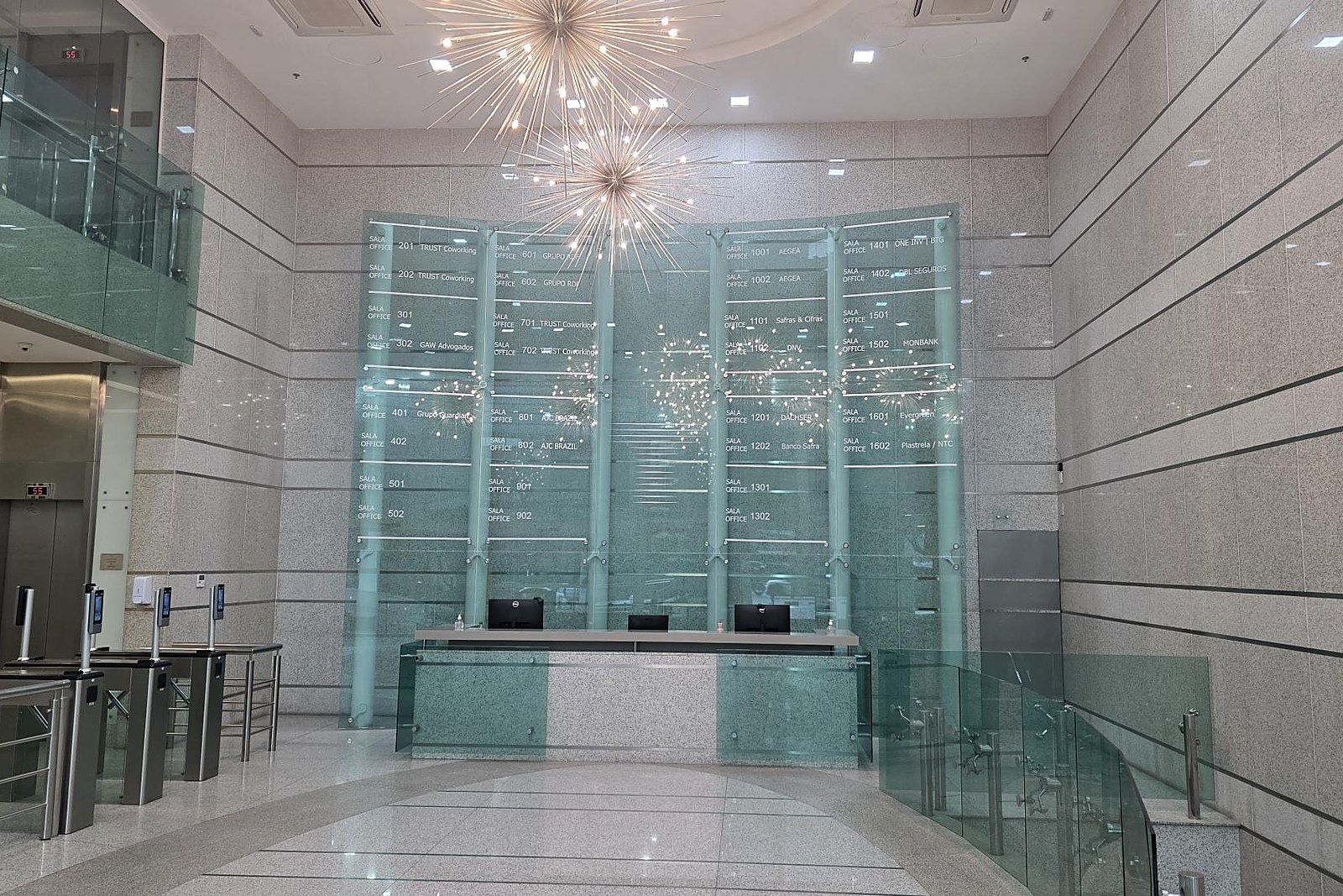 Recepção do Trust Business Center, com balcão de atendimento e o painel de vidro com a relação de salas.